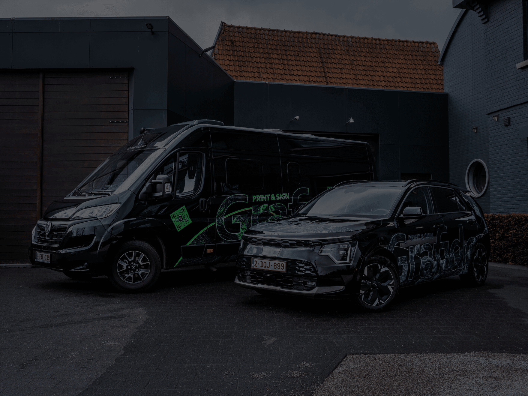Zwarte bestelwagen en SUV met groene en blauwe Grafido-voertuigwrap voor een donker modern pand